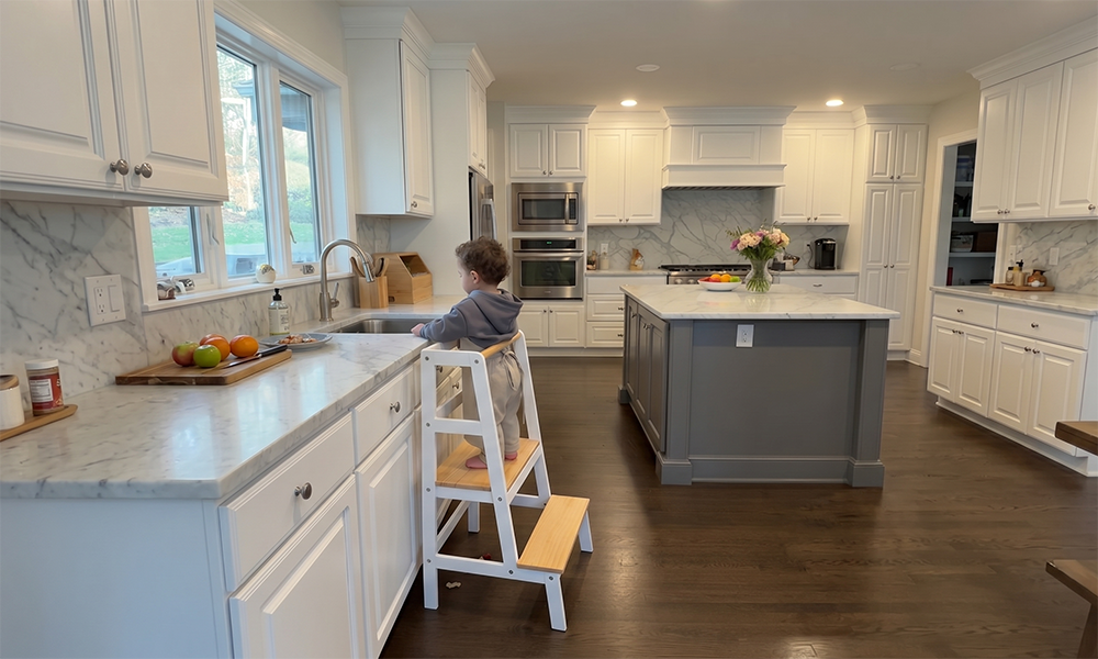 A toddler can safely and easily reach the kitchen sink on the Damoch Family Moore Toddler Kitchen Standing Tower and join in kitchen activities.