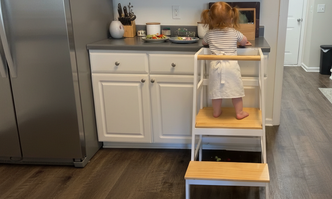 A toddler stands on the Damoch Family Moore toddler kitchen standing tower to participate in the kitchen activities